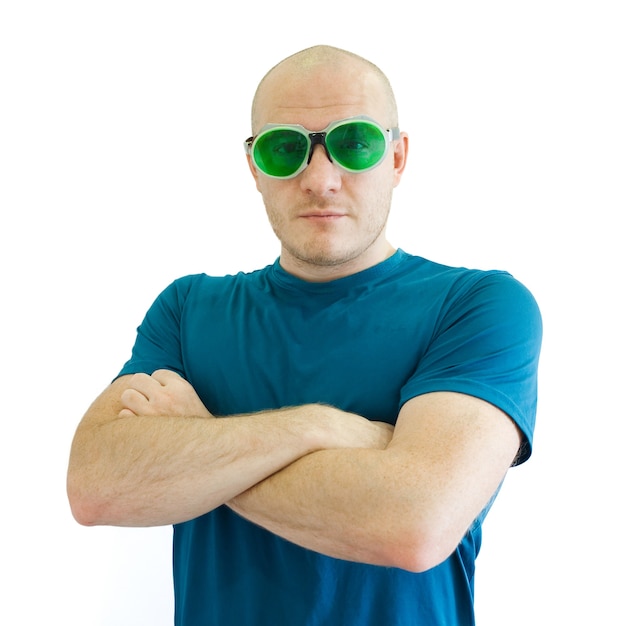 Adult caucasian bald man in blue tshirt and funny green sunglasses stands with folded hands