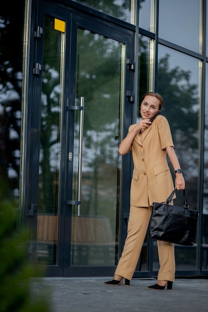 Adult Caucasian Confident Young Business Woman is Talking on Phone Outside near Modern Office Building.