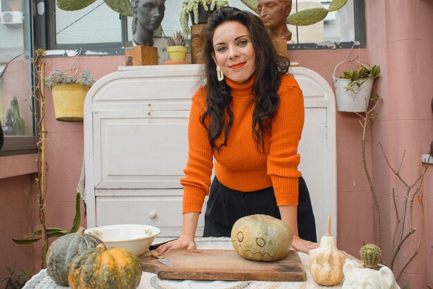 Adult caucasian woman artist decorating pumpkin for Halloween leaning on table looking at camera