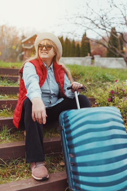 An adult Caucasian woman in a hat sunglasses and a red vest arrived at the place of settlement in rented housing Travel concept