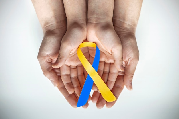 Photo adult and child hands holding blue and yellow ribbon shaped paper down syndrome awareness world down syndrome day