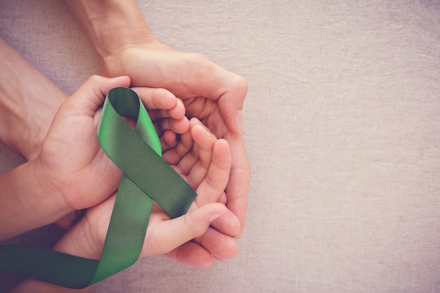 Adult and child hands holding Green Ribbon, cancer awareness