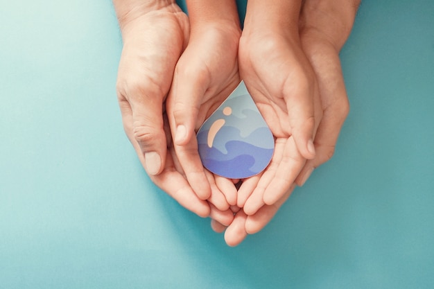 Foto le mani del bambino e dell'adulto che tengono la carta hanno tagliato la goccia di acqua. giornata mondiale dell'acqua. acqua pulita e servizi igienico-sanitari, csr, risparmiare acqua.