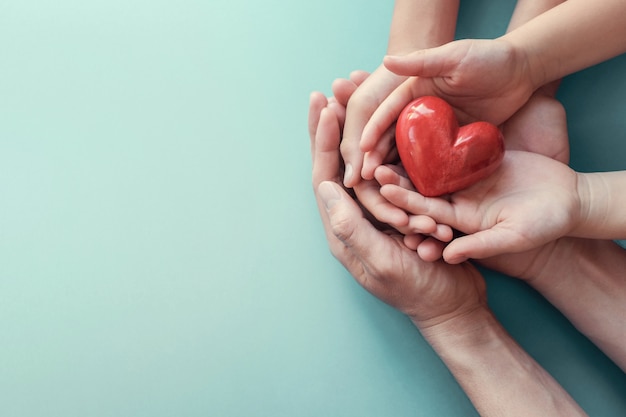 Photo adult and child hands holding red heart on aqua background