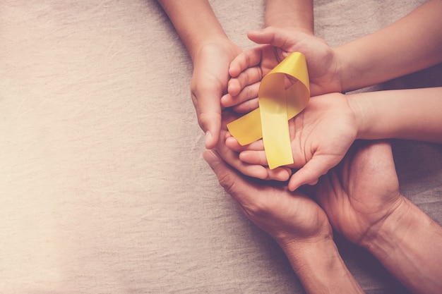 Adult and children hands holding yellow gold ribbon