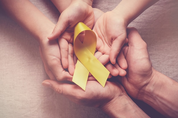 Photo adult and children hands holding yellow gold ribbon