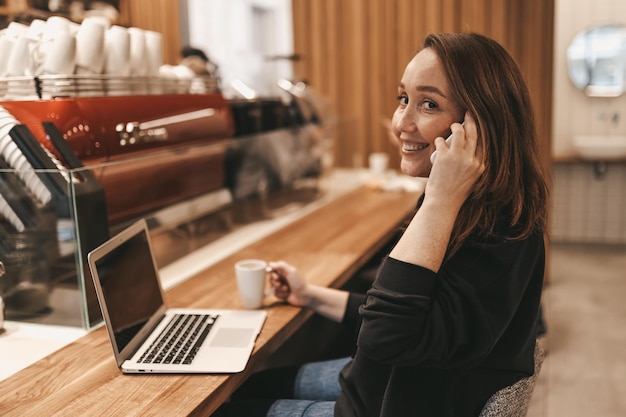 Foto adulta sorridente donna d'affari freelance che lavora in un caffè usando un portatile