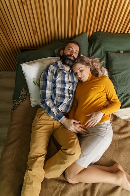 An adult couple in love waiting for a child. A man and his pregnant wife are basking in a bed in the bedroom