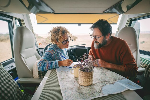 Coppia adulta che pianifica la prossima destinazione di viaggio seduta all'interno di un camper utilizzando una guida mappa cartacea