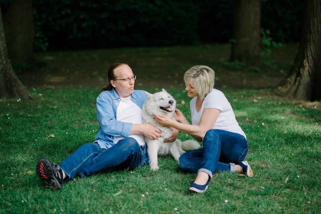 Adult couple sitting on the grass with a white dog