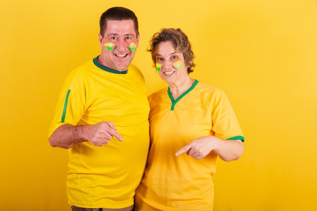 Adult couple soccer fan from brazil pointing to center only\
here advertising photo