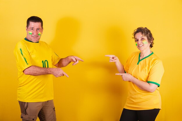 Adult couple soccer fan from brazil pointing to the center
together advertising photo