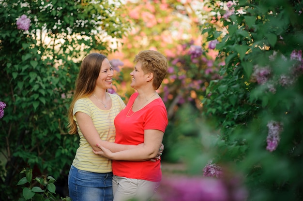 Adult daughter hugs her older mother outdoors in the park.