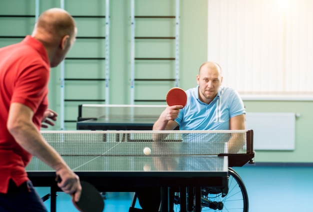 Adult disabled man in a wheelchair play at table tennis with his coach