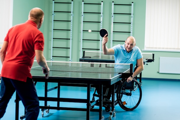 Adult disabled man in a wheelchair play at table tennis with his coach