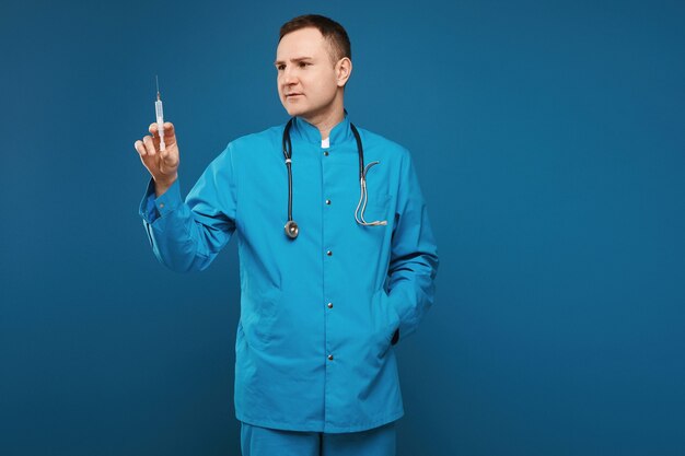 Adult doctor in blue medical uniform holding a medical syringe for injection, isolated on blue