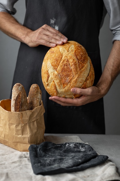 An adult european male baker holds a round fresh bread in his hands a man in a bakery holds a