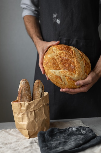 Взрослый европейский пекарь держит в руках круглый свежий хлеб, а мужчина в пекарне держит