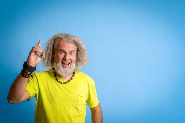 Adult excited bearded hipster man in casual yellow shirt standing holding index finger up with great new idea looking at camera isolated on pastel blue background