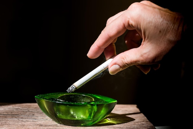 Adult female hand flicking cigarette ash into green ashtray black background