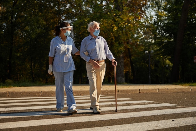 Adult friendly woman medicine worker walking with old man in the city