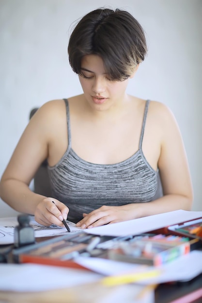 adult girl draws on paper pencils / portrait of a beautiful young female student, art school education, concept of art education