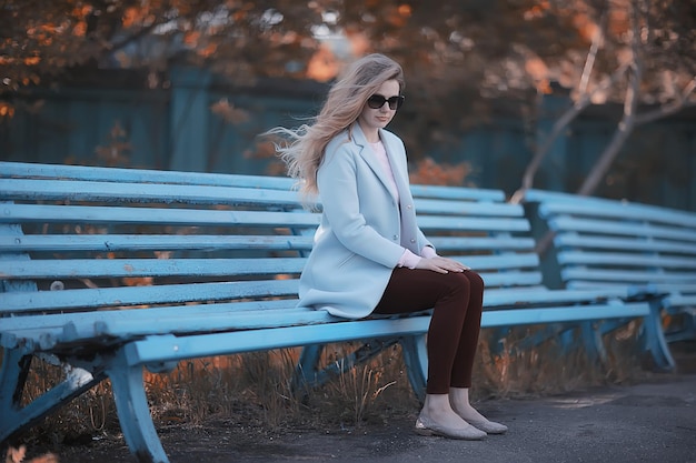 adult girl sitting on a bench in the park / beautiful model woman resting on a bench, cheerful happy girl