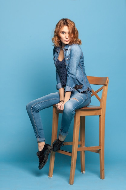 Adult girl sitting on a chair on blue