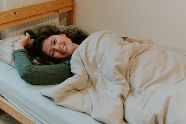 Foto una ragazza adulta si sveglia e si sdraia a letto con un sorriso felice.