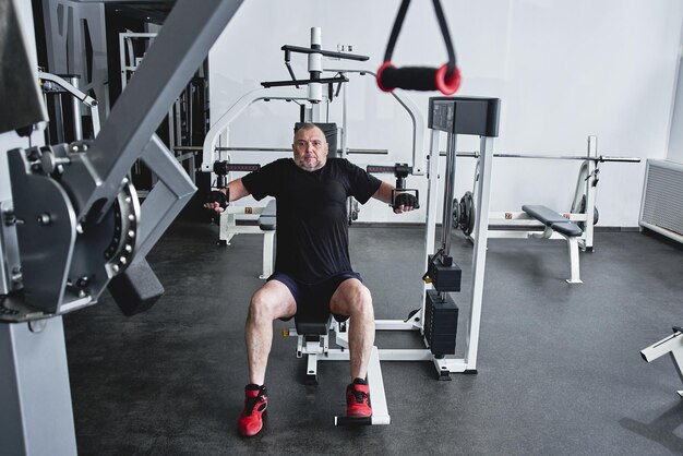 성인 회색 머리 남자는 체육관 펌프 다리와 팔 근육에서 피트니스 장비에서 훈련 노년의 건강한 생활 방식의 개념에서 무게를 잃는다