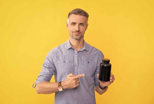 Adult guy pointing finger on drug jar on yellow background food additive
