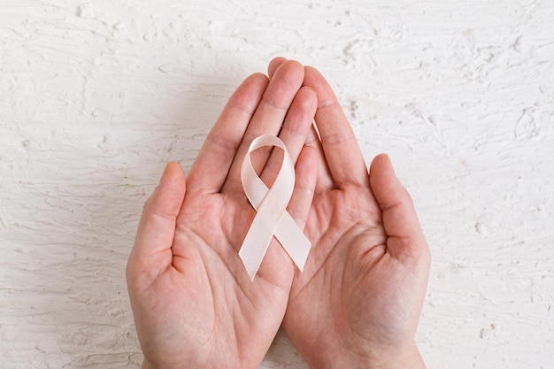 Взрослые руки держат персиковую ленту Месяц осведомленности о раке матки Здравоохранение и Всемирный день борьбы против рака