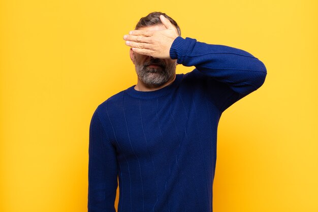 Adult handsome man covering eyes with one hand feeling scared or anxious, wondering or blindly waiting for a surprise