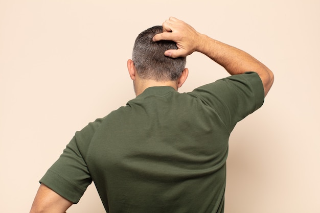 adult handsome man feeling clueless and confused, thinking a solution, with hand on hip and other on head, rear view