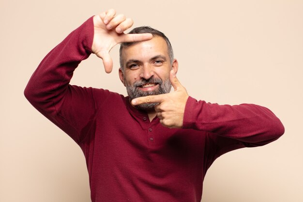 Adult handsome man feeling happy, friendly and positive, smiling and making a portrait or photo frame with hands