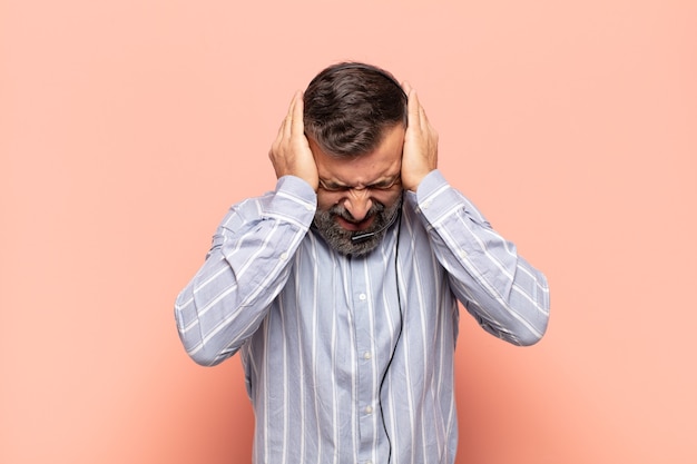 Bell'uomo adulto che si sente stressato e frustrato, alza le mani alla testa, si sente stanco, infelice e con emicrania