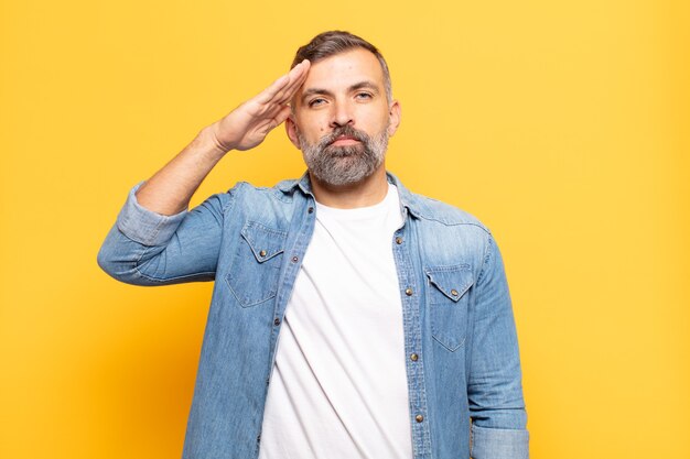 Adult handsome man greeting with a military salute in an act of honor and patriotism, showing respect