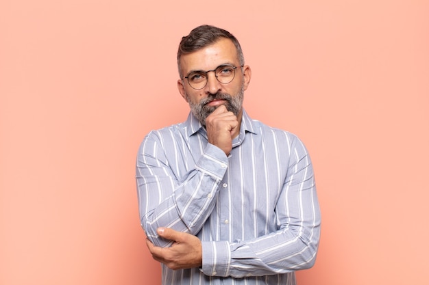 Adult handsome man looking happy and smiling with hand on chin, wondering or asking a question, comparing options