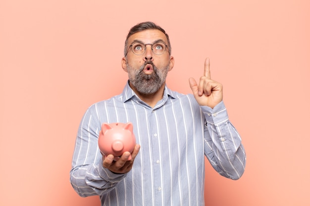 Adult handsome man looking shocked, amazed and open mouthed, pointing upwards with both hands to copy space