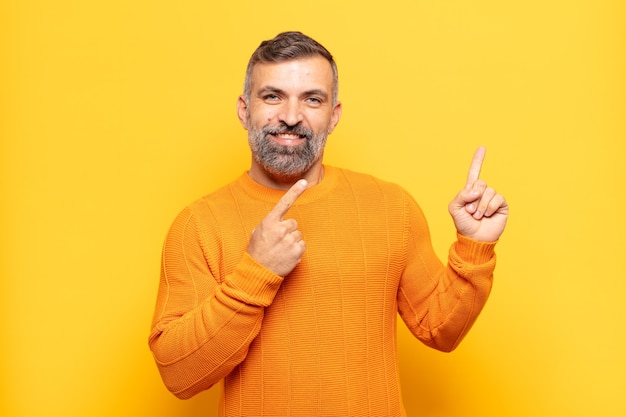 Adult handsome man smiling happily and pointing to side and upwards with both hands showing object in copy space