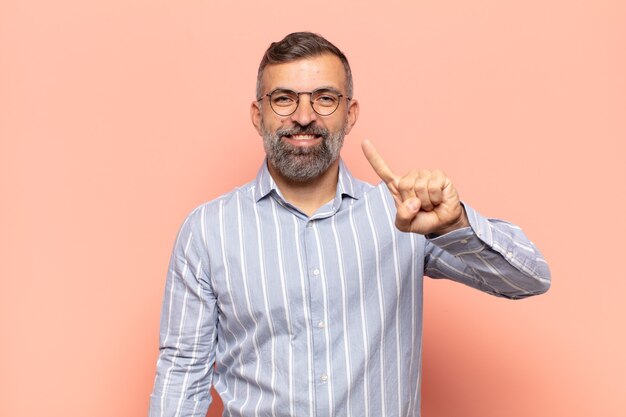 Adult handsome man smiling and looking friendly, showing number one or first with hand forward, counting down