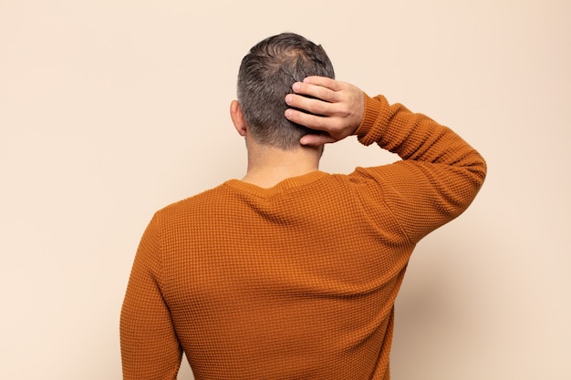 考えたり疑ったり、頭を掻いたり、困惑したり混乱したりする大人のハンサムな男、背面図または背面図