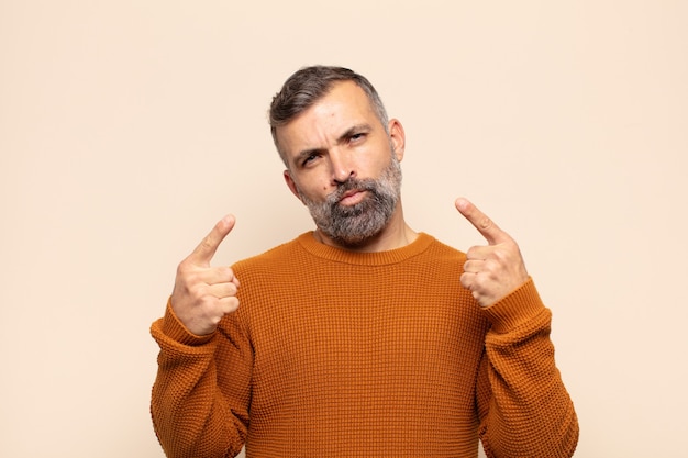 Adult handsome man with a bad attitude looking proud and aggressive, pointing upwards or making fun sign with hands