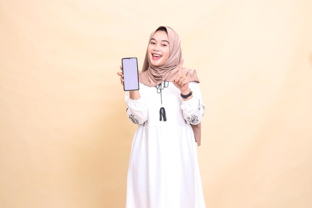 an adult indonesia Muslim woman wearing a hijab with a cheerful smile displays a cellphone gadget sc