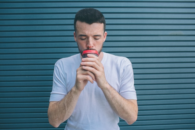 Adult is holding cup of coffee close to mouth. He is keeping eyes closed. Isolated on striped 