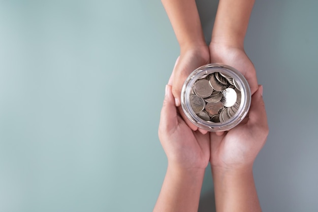 Взрослые и детские руки держат банку с монетами и концепцию сбережений и пожертвований