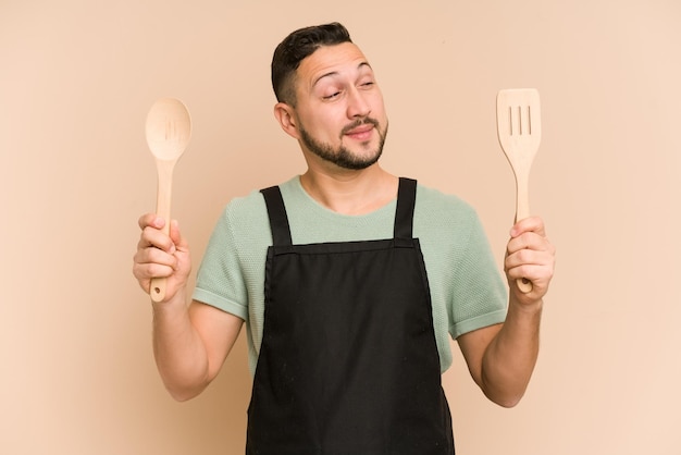 Adult latin cook man holding wooden utensils isolated