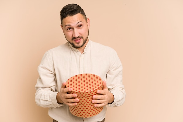 Adult latin man holding a valentines day gift isolated