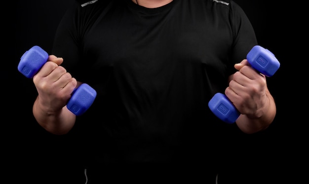 Adult male athlete in black uniform holds blue plastic blue dumbbells