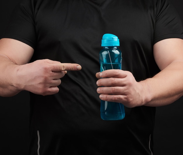 Adult male athlete with muscles holds a plastic bottle of water